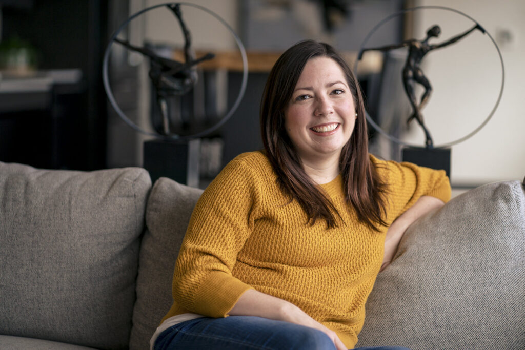 A picture of a woman in a yellow sweater sitting on a sofa smiling at the camera. 