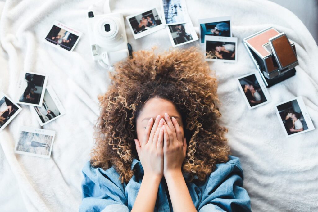 A picture of a woman covering her face with her hands, surrounded by polaroid pictures. 