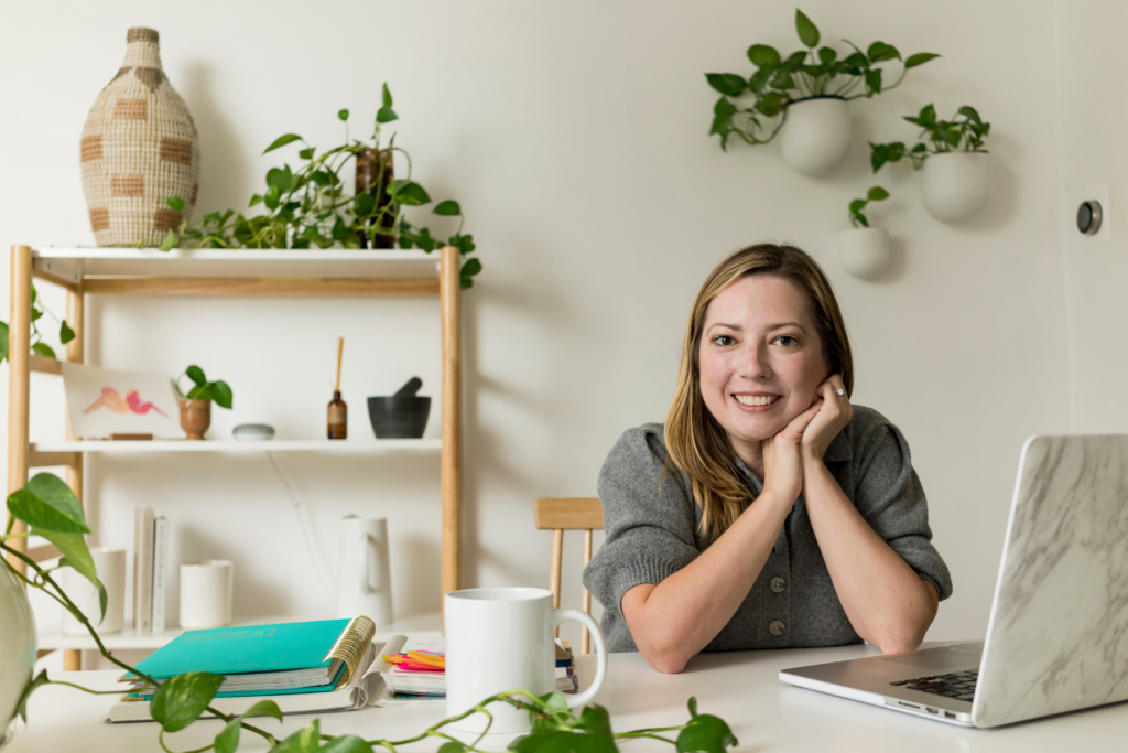 A posed picture of a woman sitting at a desk behind a laptop. 