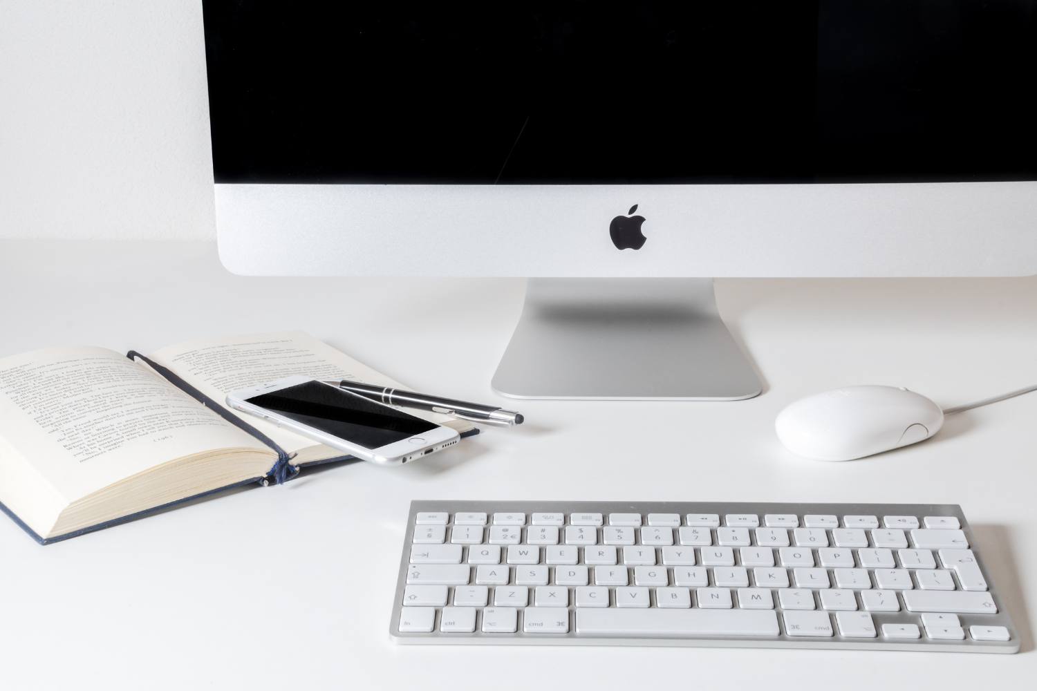 A picture of an iMac, keyboard, mouse, an iPhone sitting on a white desk. 